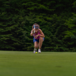 Woman golferr kneeling and sizing up a putt on the green of Hawk's Eye GC.