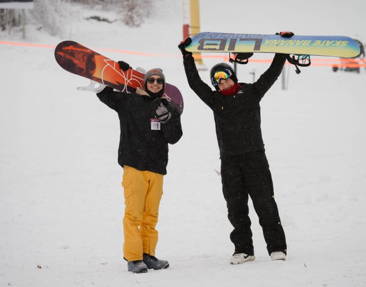 Two snowboarders holding their snowboards and posing in front of the yellow chairlift