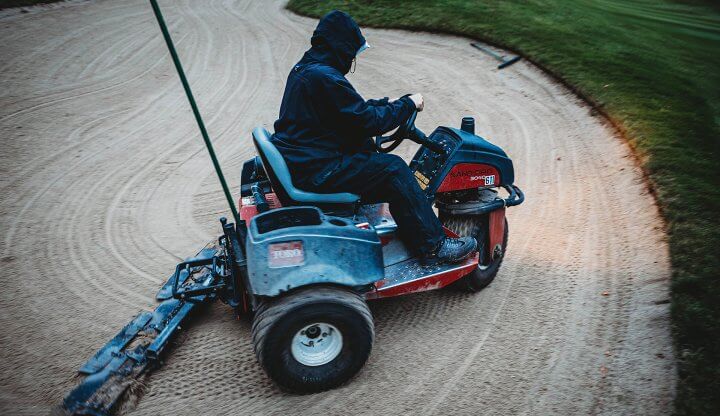 Golf Maintenance Team Member Driving Sand Pro in Sand Bunker on Golf Course