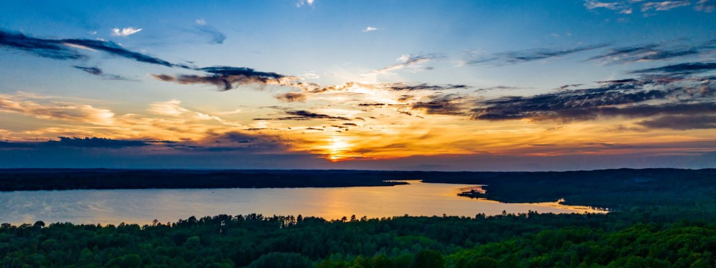 Aerial shot of the sunset over Lake Bellaire with the woods in the foreground