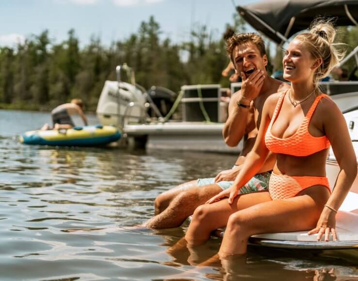 A male and female couple in their bathing suits sit on the back of a boat in the Grass River