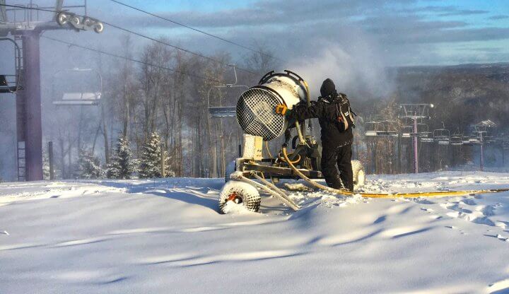 Snowmaker pointing snow gun atop Schuss Mountain towards purple chairlift