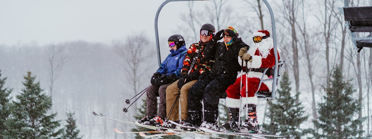 Skiing Santa sitting on a chairlift with 3 other skiers at Schuss Mountain