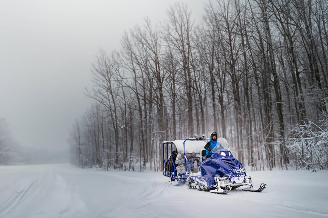 Shanty Creek Employee Driving Snowmobile Hauling the Snow Glide Trailer behind it giving a scenic winter tour.