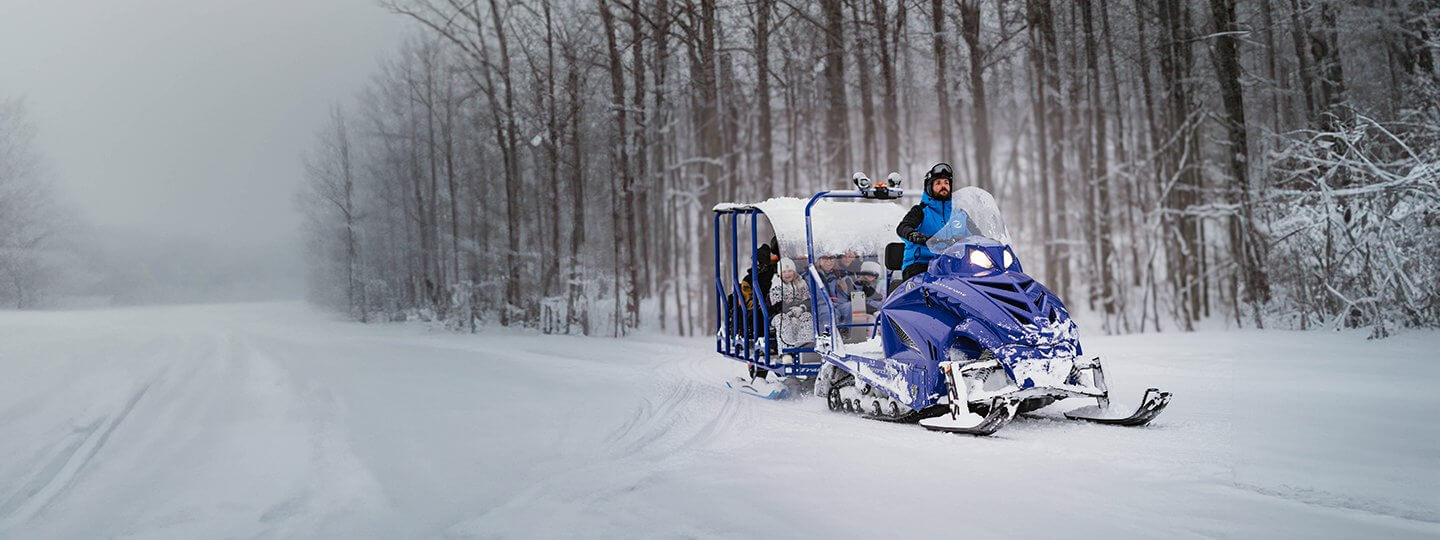 Shanty Creek Employee Driving Snowmobile Hauling the Snow Glide Trailer behind it giving a scenic winter tour.